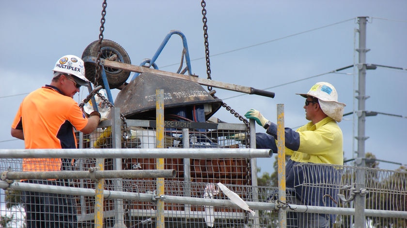 Two constructions unload items from a steel cage being lowered by a crane, including an upside down wheelbarrow