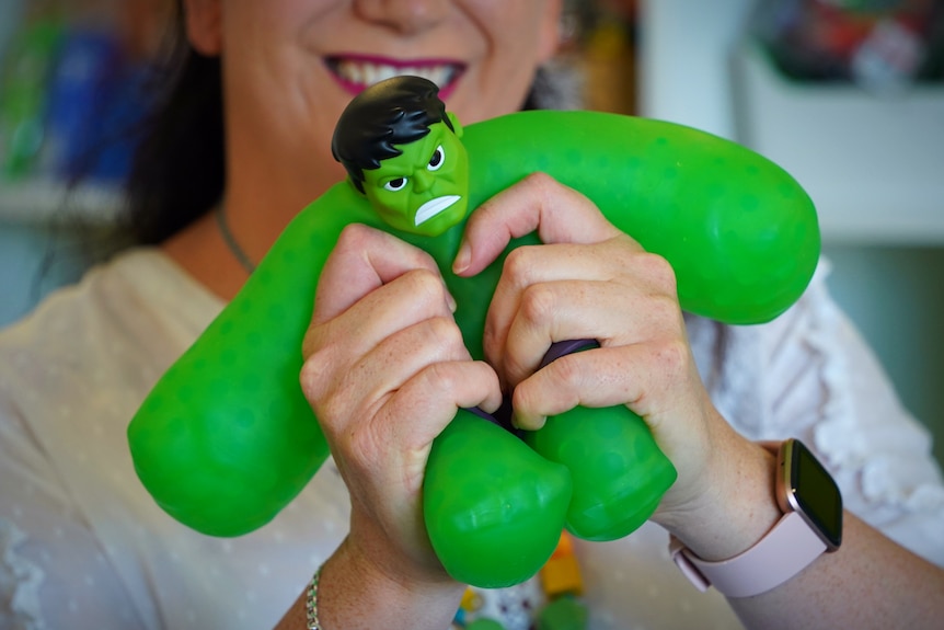 A woman holds a stretchy green hulk action figure toy in front of her