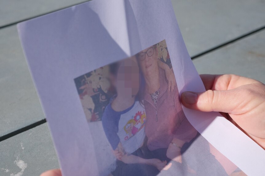 A woman holds a photo of herself sitting next to her daughter, who has her armed draped over her shoulder