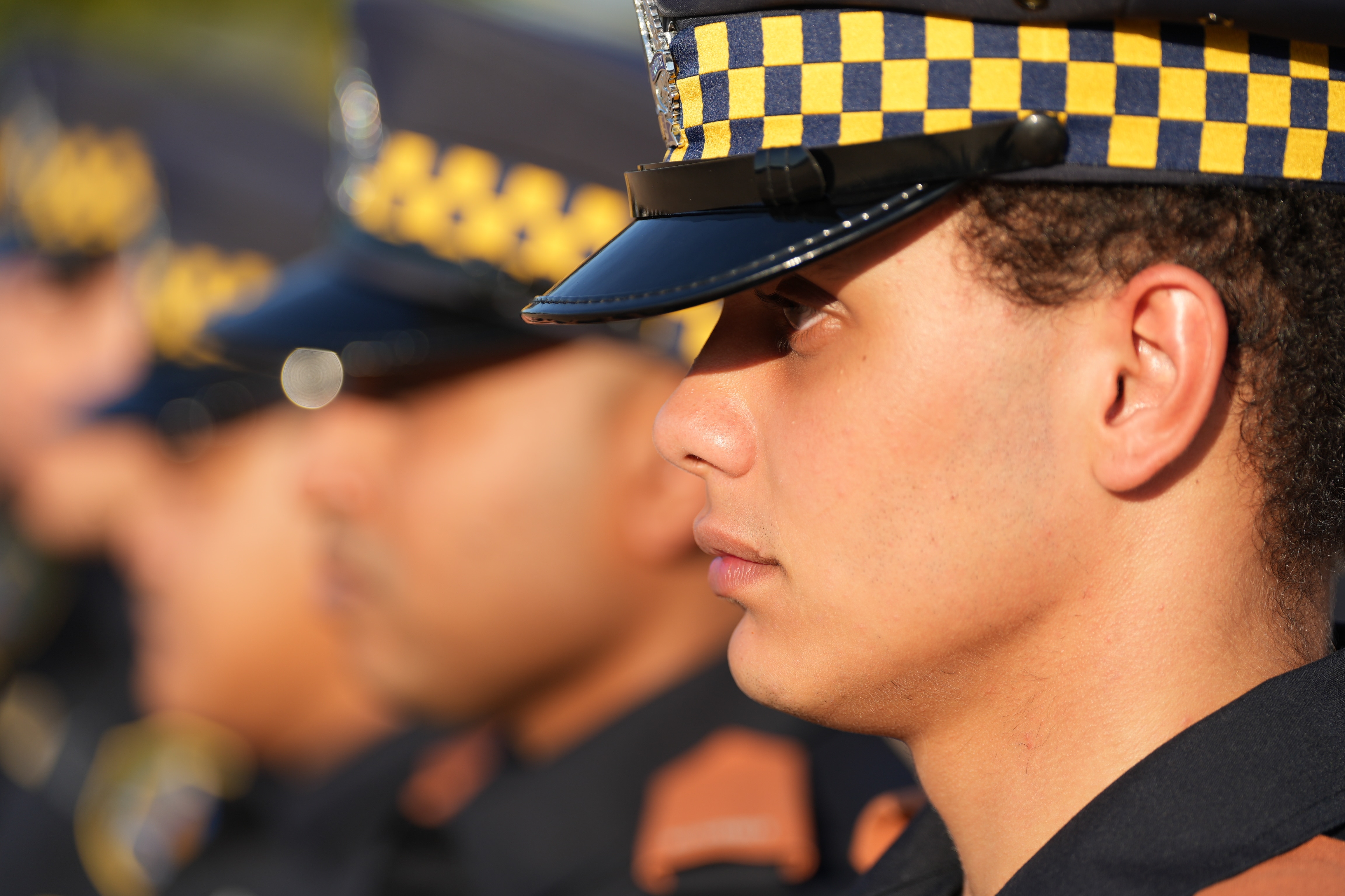 A side profile of a man wearing a police hat with other officers in the background.