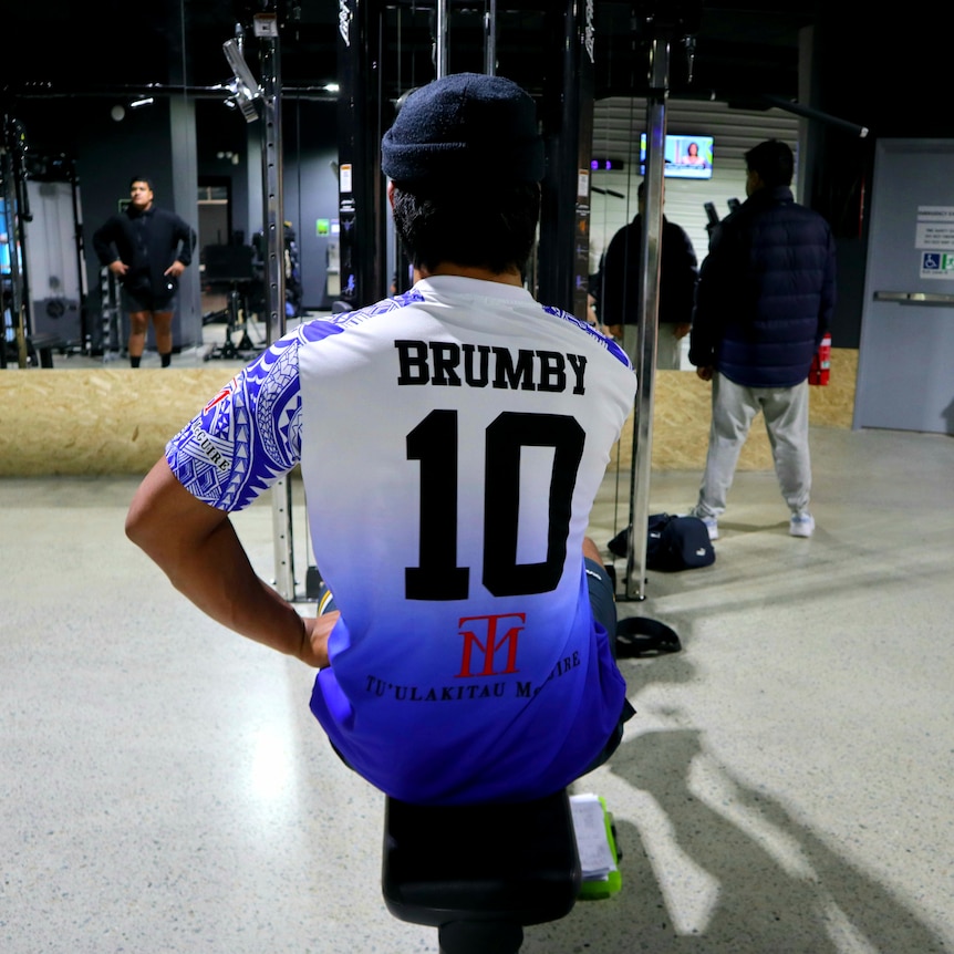 The back of a male wearing a Brumby shirt on an exercise machine