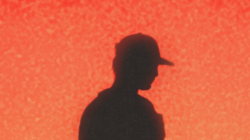 A silhouette of Joji from the torso up against a red/orange, grainy background