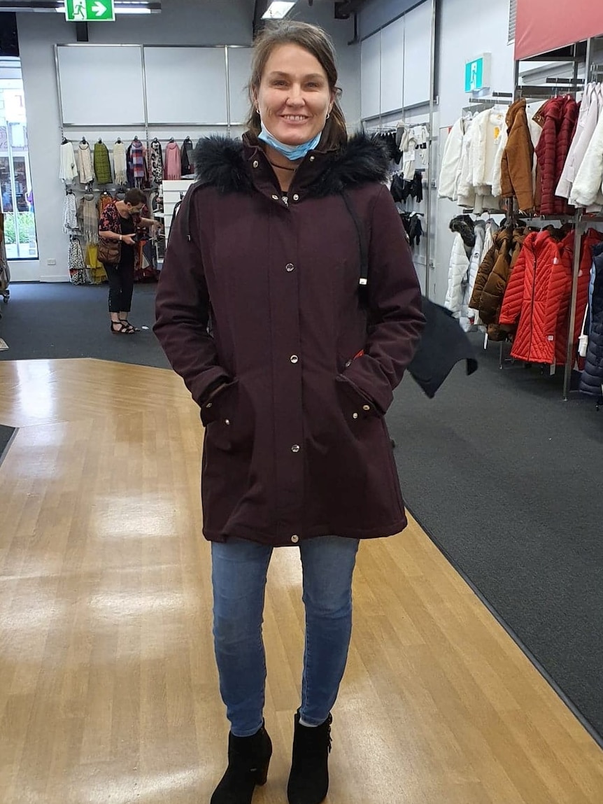 Tamra smiles for a photo in a clothes shop, a face mask lowered around her chin.