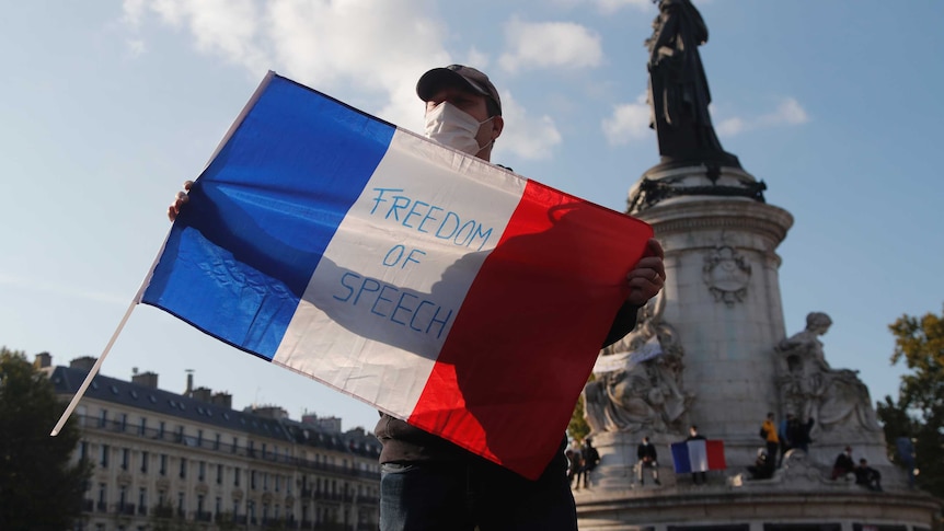 A man holds a French flag which bear the words 'freedom of speech'.