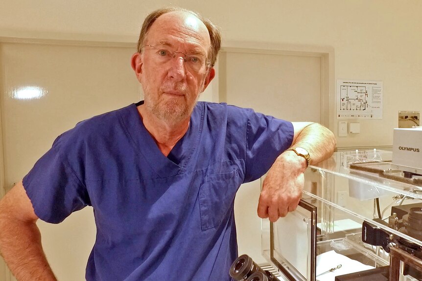 Professor Rob Norman, wearing surgical scrubs, stands next to medical equipment.