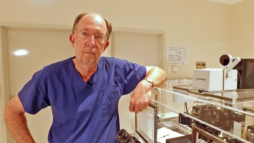 Professor Rob Norman, wearing surgical scrubs, stands next to medical equipment.