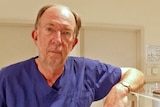 Professor Rob Norman, wearing surgical scrubs, stands next to medical equipment.
