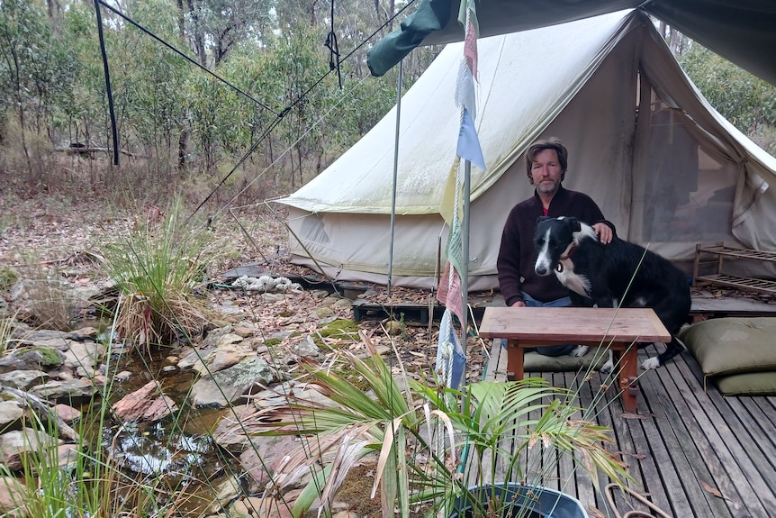 A man and his dog sitting outside a tent.