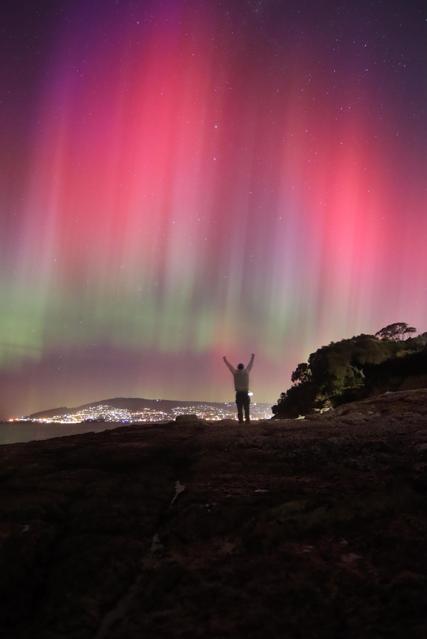 Purple and pink lights in the sky with someone raising their arms to the air in the foreground.