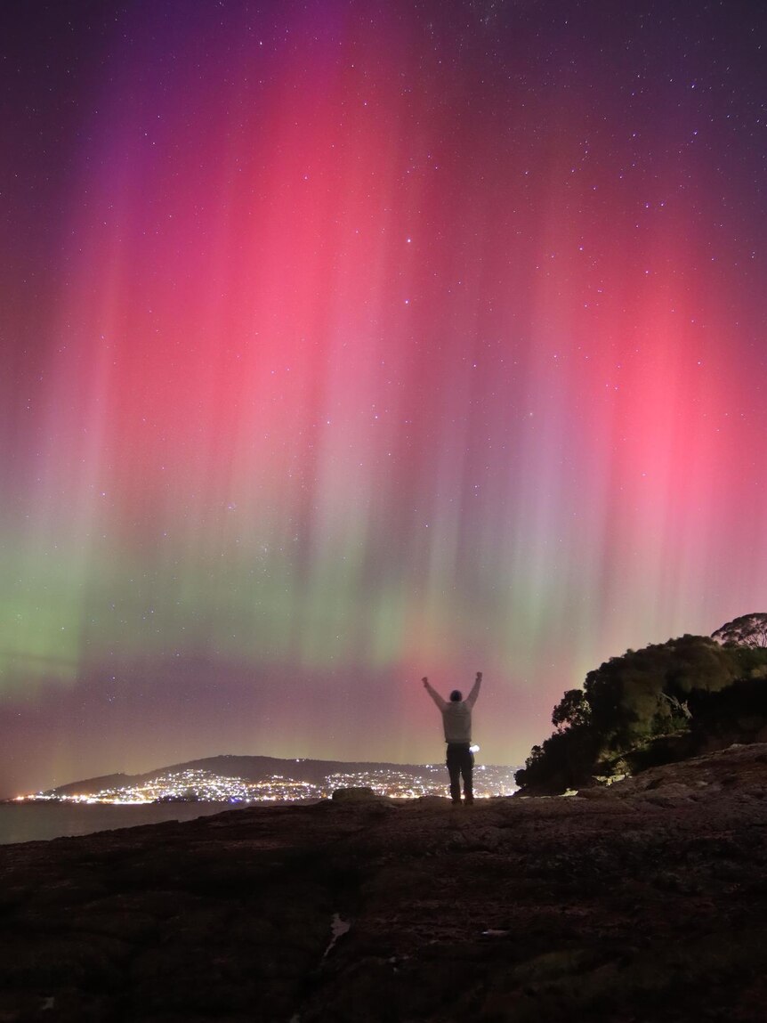 Purple and pink lights in the sky with someone raising their arms to the air in the foreground.