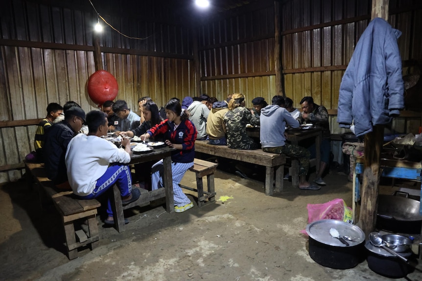 Dozens of people sit at dinner tables together on a dirt floor