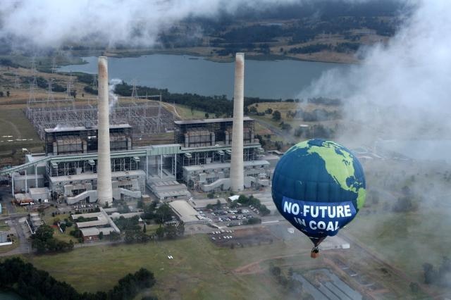 A hot air balloon featuring the words ‘Save the climate - No future in coal’ flies over a power station.