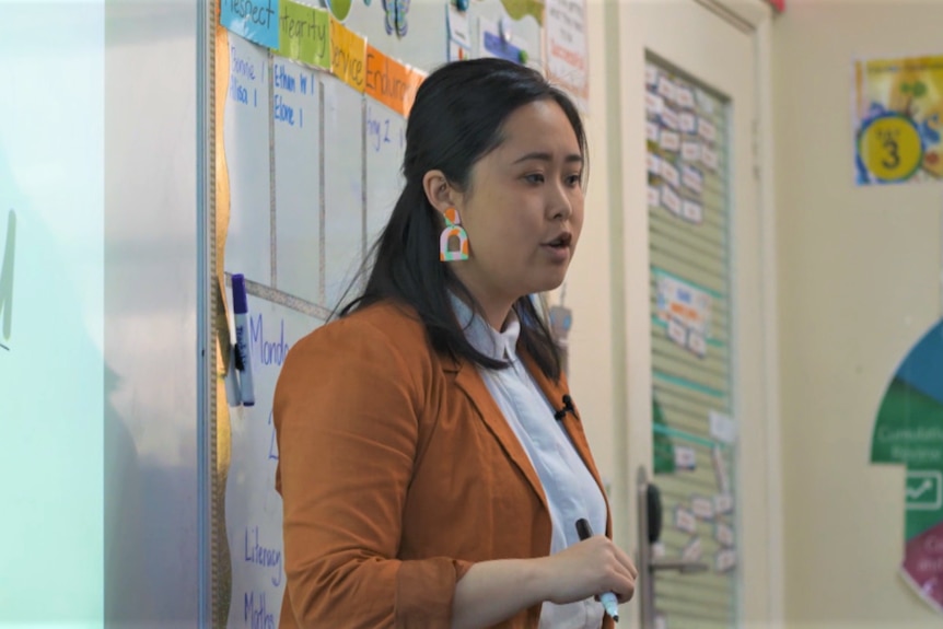A young Asian woman with black hair standing in front of a classroom whiteboard