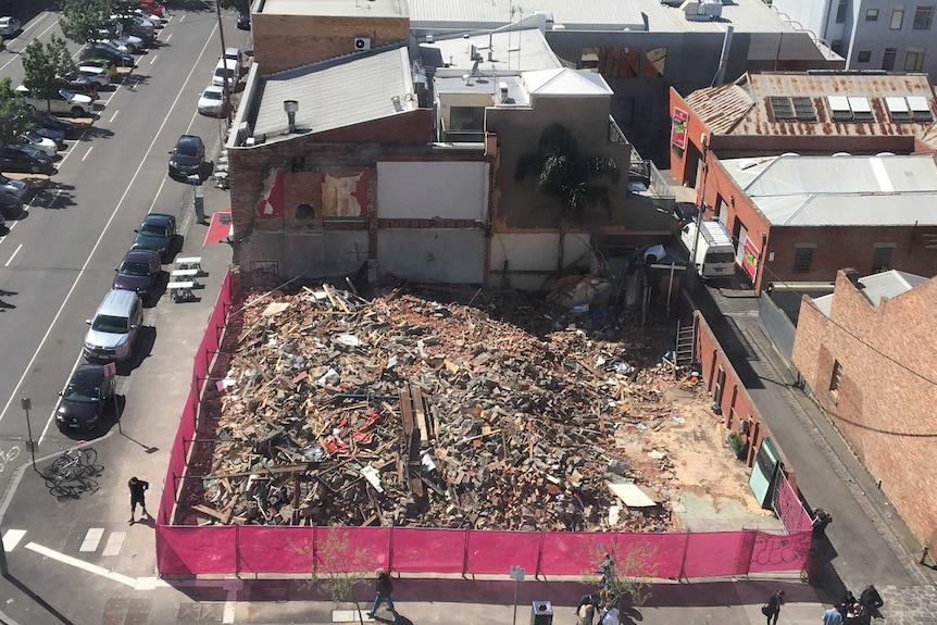 Purple fencing surrounds a large pile of rubble in a suburban setting.