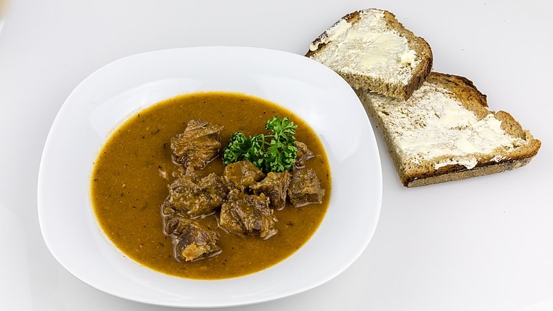 Oxtail soup in a bowl next to two pieces of sliced bread and butter