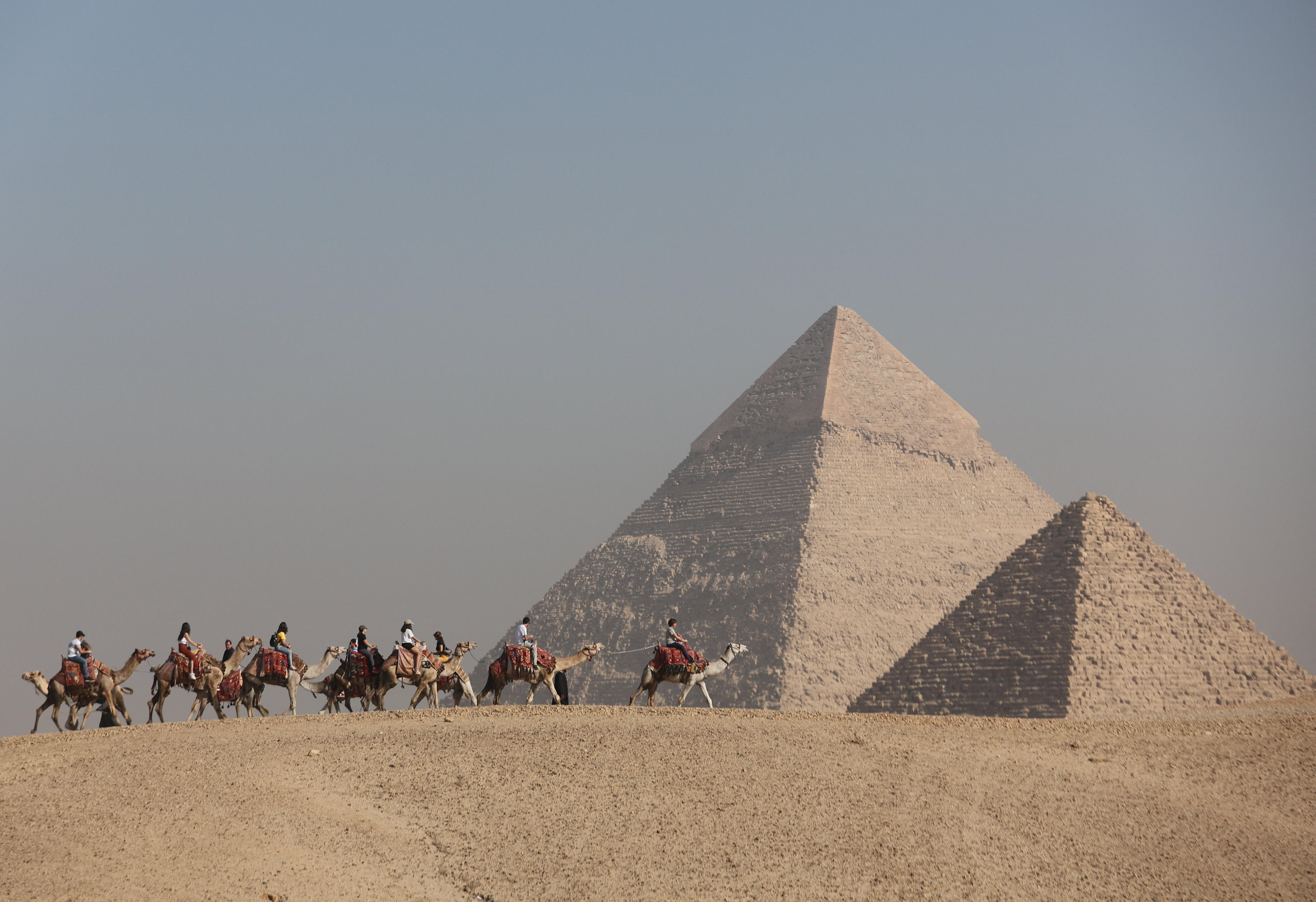 People ride horses between one large and one smaller pyramid.
