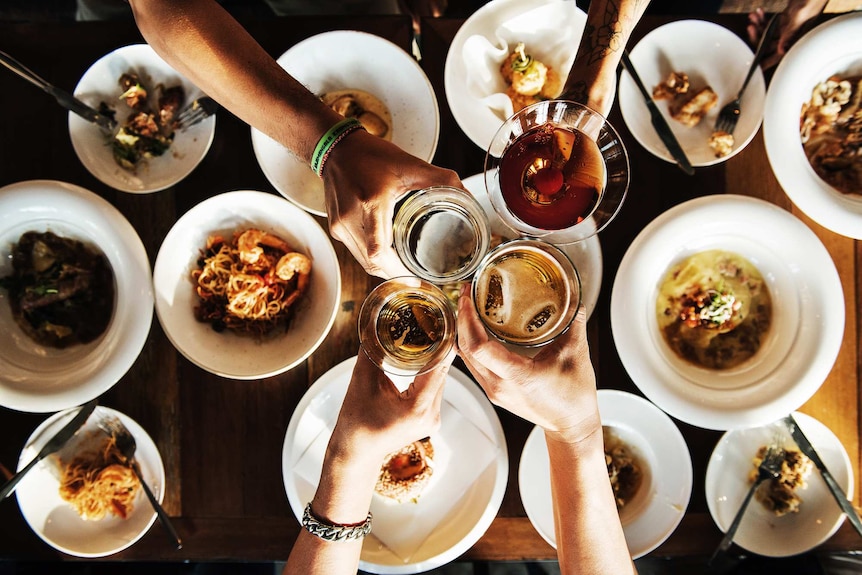 Top down shot of four toasting alcoholic drinks above a dinner table to illustrate dinner party.