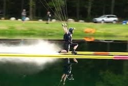 A man suspended from a parachute skids along the surface of the water on a pond with demarcated lanes.