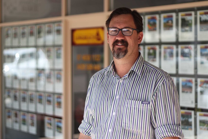 Man with glasses standing in front of a real estate office