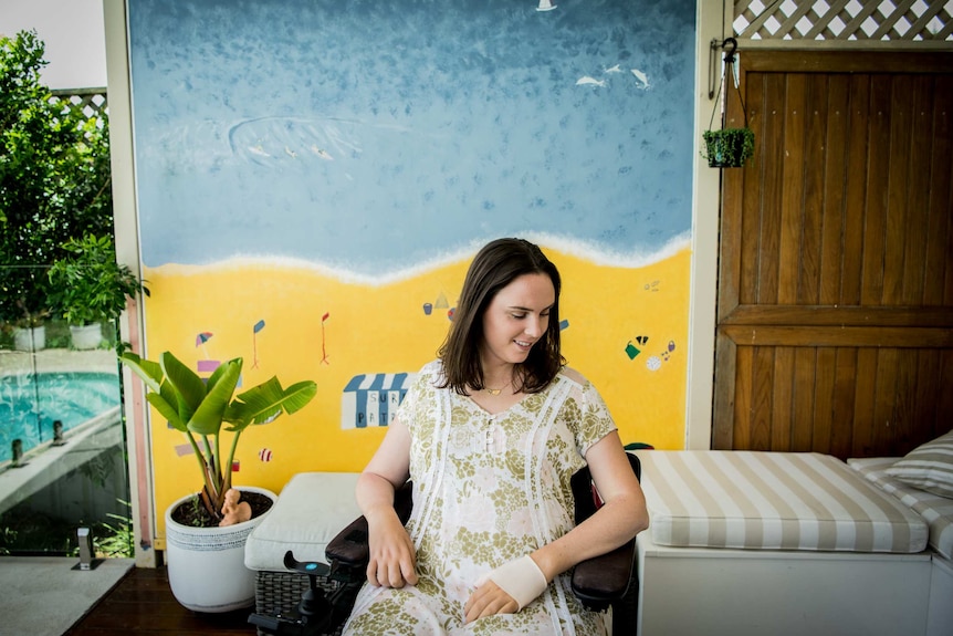 Jess Collins sits in her home in front of a mural she and her siblings painted as children of the beach.