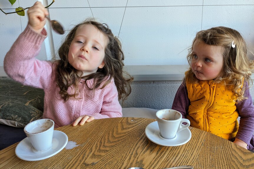 Two little girls drink milky coffees and make a mess.