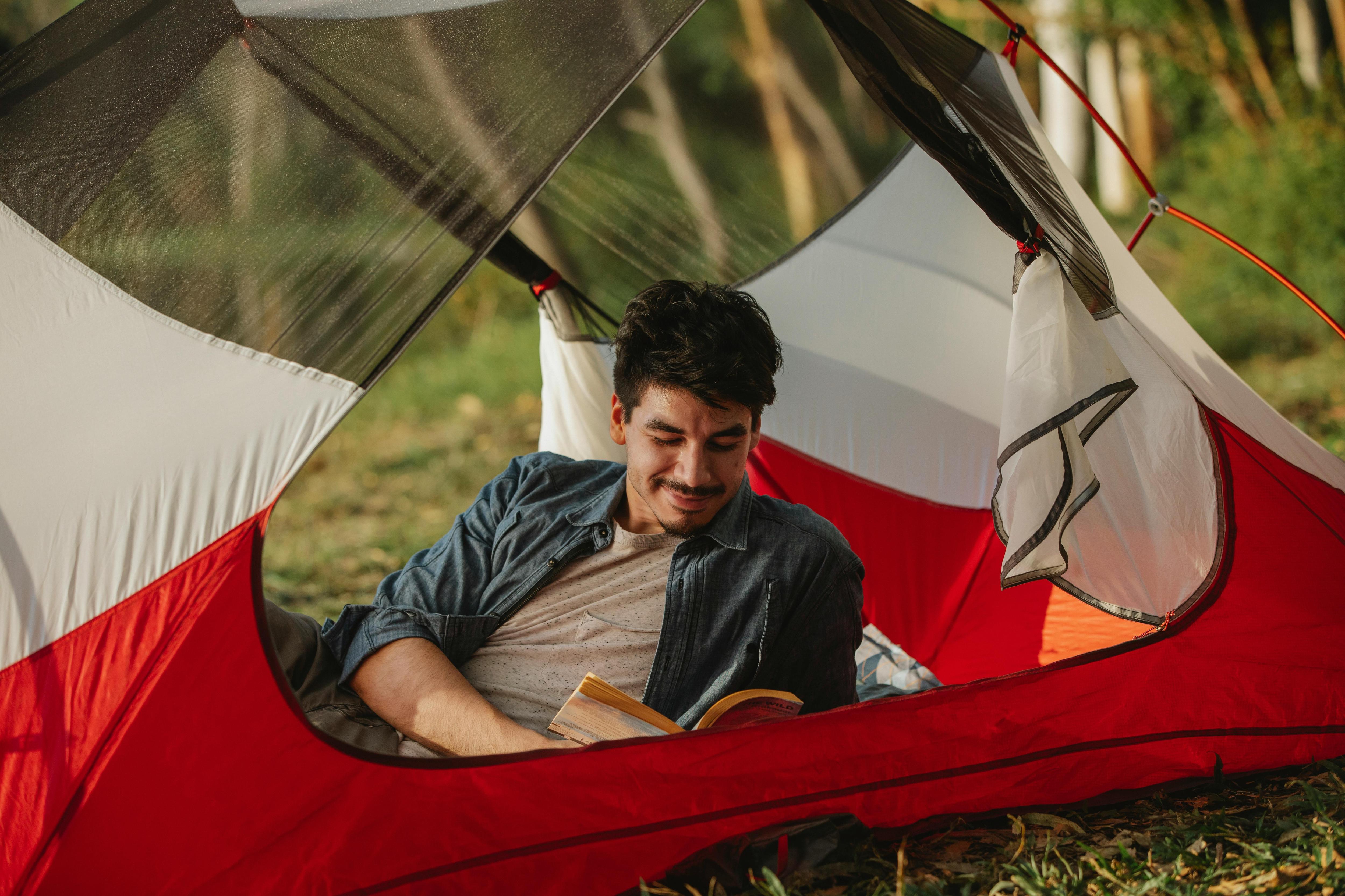 young man reading a novel in a tent