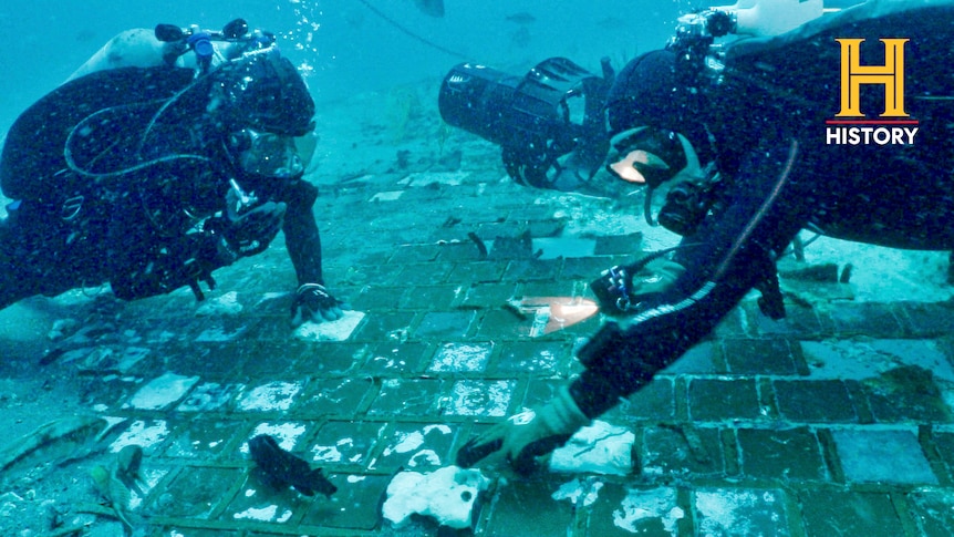 Two divers float over a tiled panel on the ocean floor