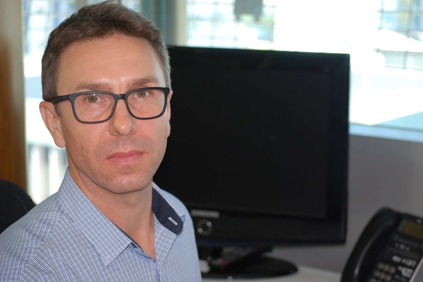 Jason Corbett is seen form close range wearing glasses in an office in front of a blank computer screen.