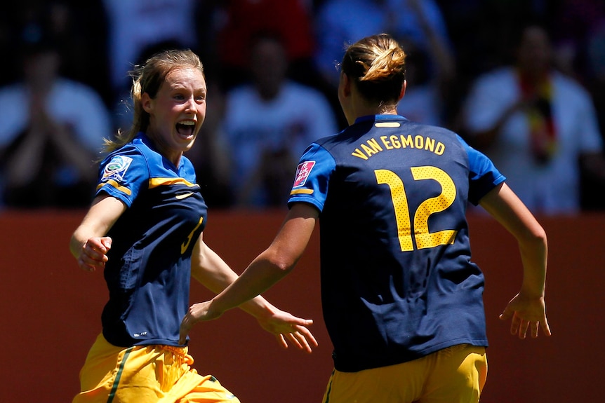 Ellyse Perry celebrates scoring a goal with her arms out wide alongside teammate Emily Van Egmond
