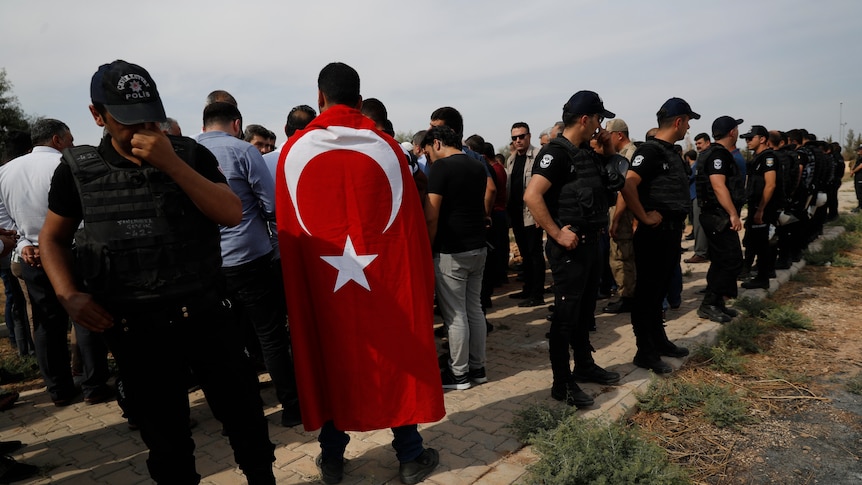 Turkish police officers secure the area as a Turkish flag-draped mourner attends a funeral.