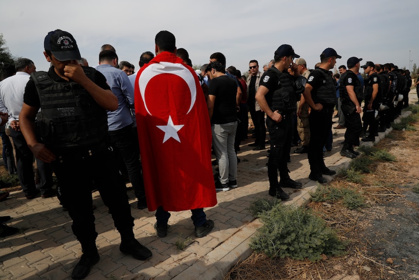 Turkish police officers secure the area as a Turkish flag-draped mourner attends a funeral.