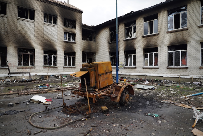 Destroyed equipment sits outside the burnt out shell of a school.