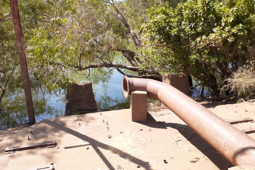 a large rusted metal pipe above a creek lined with trees