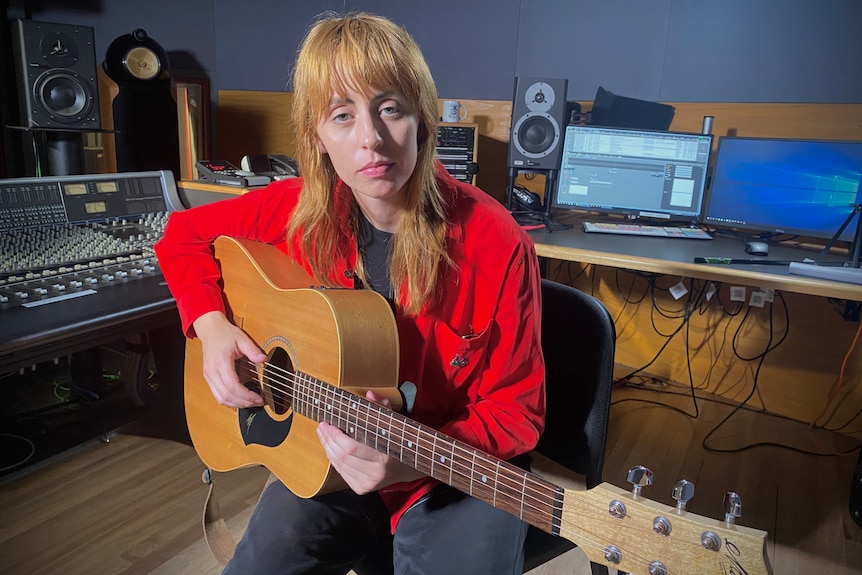 Sophie Payten AKA Gordi, an Australian musician, poses for a photo in a recording studio holding a guitar.