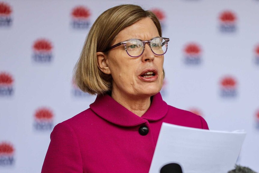 A woman standing in front of microphones while holding a piece of paper