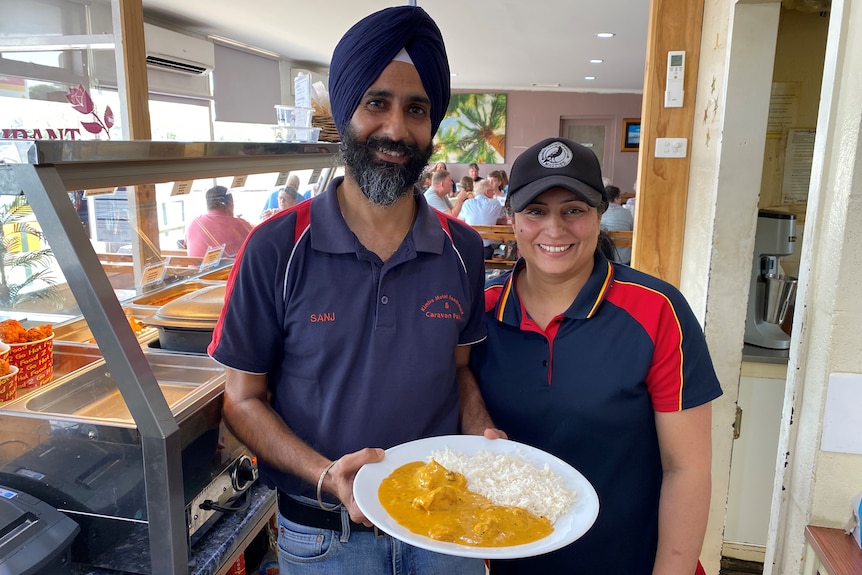 Indian Sikh man left and woman right holding plate with curry and rice in front of bain marie