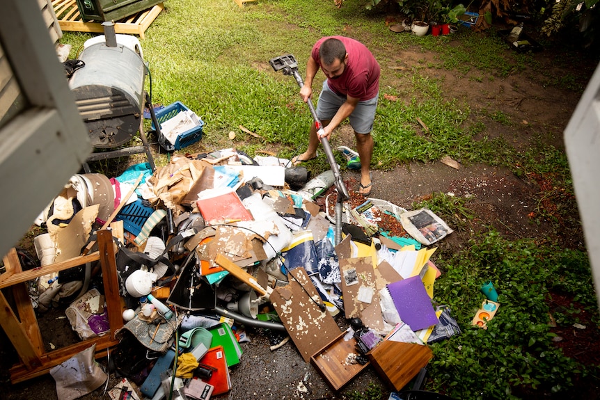 A top view of a man dropping part of a vacuum cleaner into a pile of flood damaged household items and debris piled in a yard 