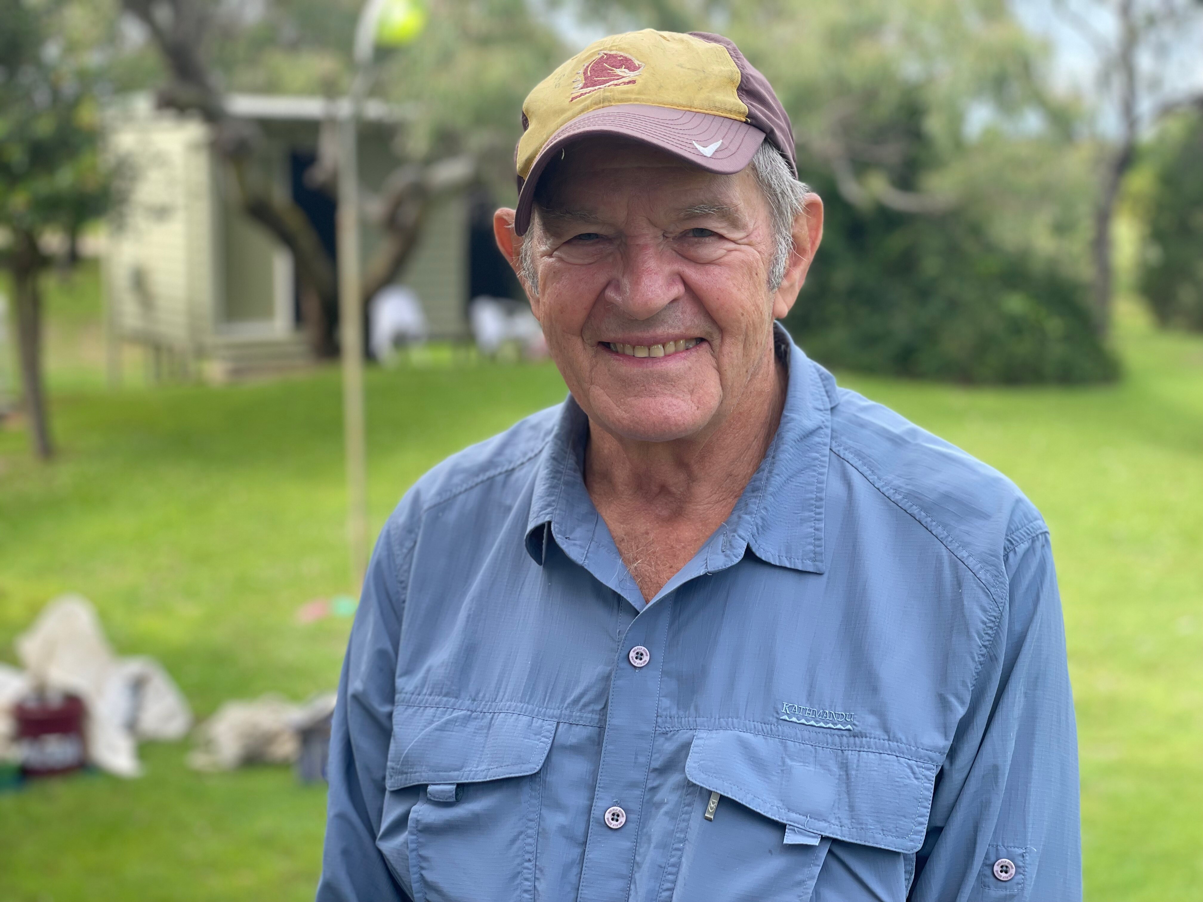 An elderly man in a blue shirt and a broncos cap smiles.