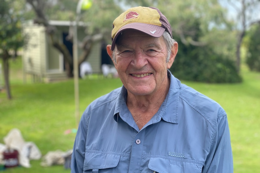 An elderly man in a blue shirt and a broncos cap smiles.