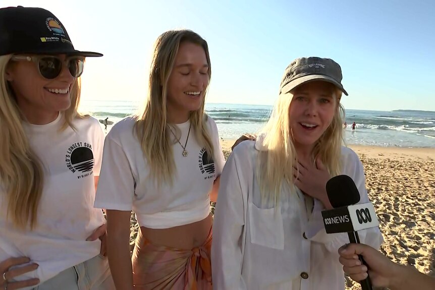 Three blonde girls on a beach talking to an ABC-branded microphone