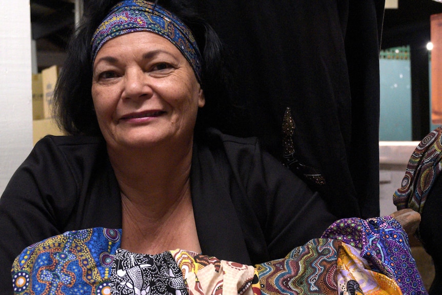 A woman sits behind a pile of brightly coloured fabric.