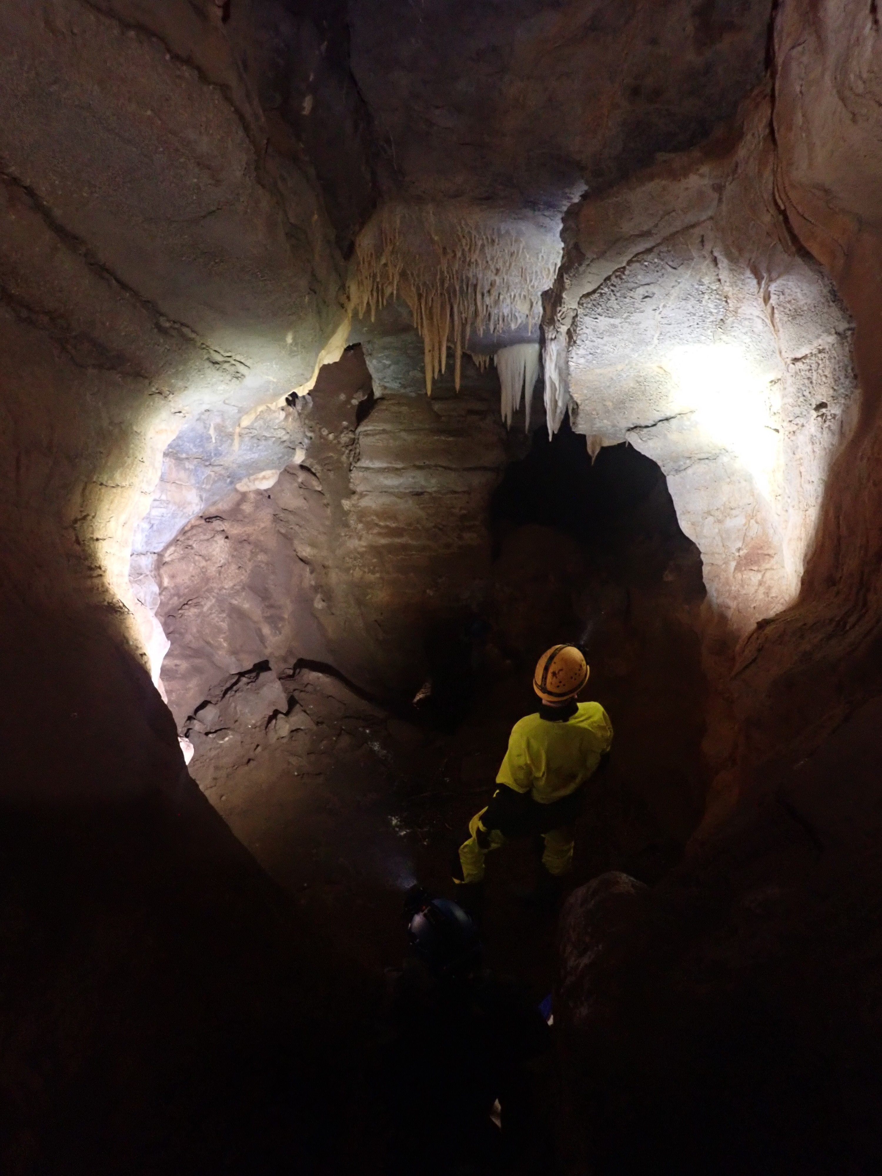 A man in caving equipment standing inside a cave that is illuminated by torch light