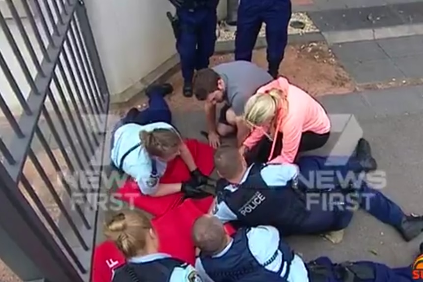 Four people hold a wally down on a red blanket.