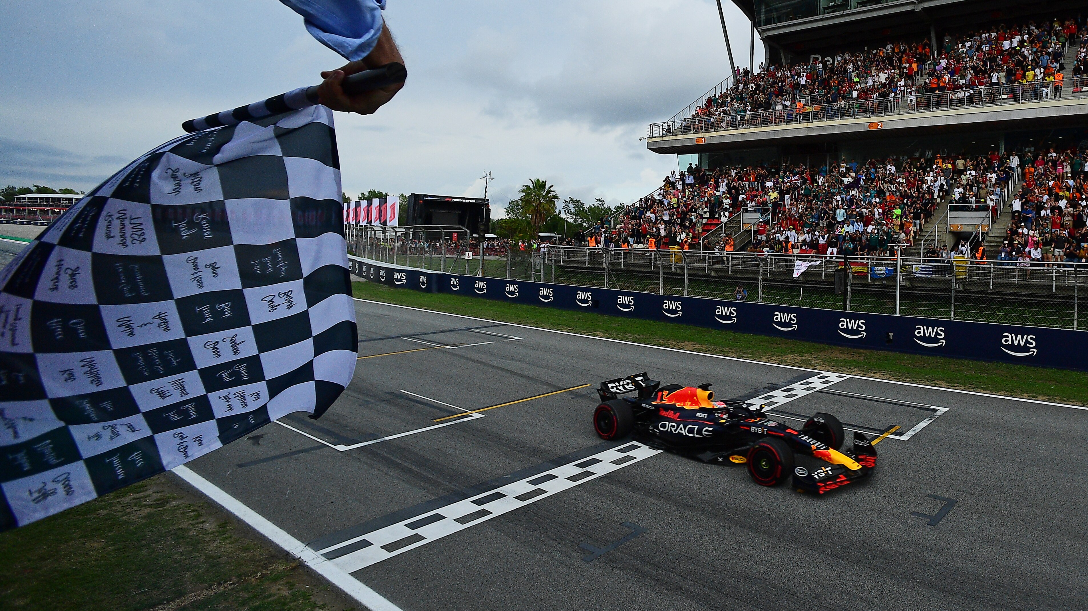 A chequered flag is waived as Max Verstappen crosses the finish line in front of a packed grandstand