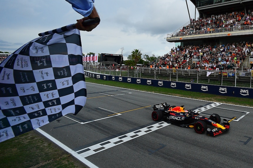 A chequered flag is waived as Max Verstappen crosses the finish line in front of a packed grandstand