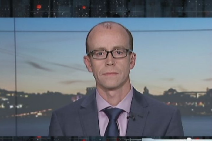 A headshot of a bald man with glasses, wearing a suit.