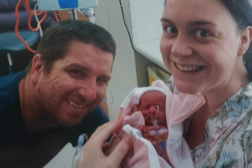 Two parents hold their baby in an hospital neonatal intensive care unit.