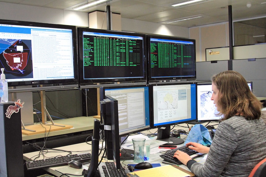 A woman sitting at a desk with seven monitors in front of her