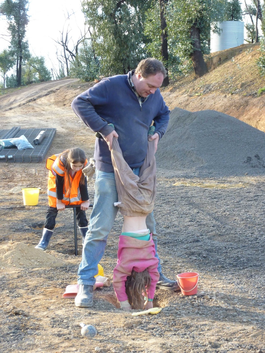 A young girl does a handstand with her feet held up by her dad