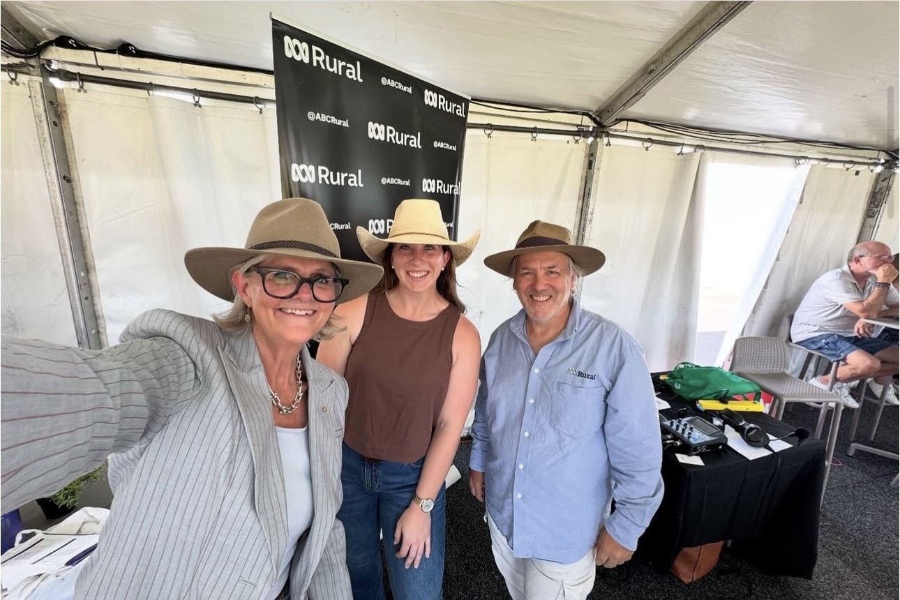 Two women and a man all in hats smile to camera.